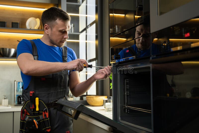 Experienced Foreman Fixes Oven Using Screwdriver in Kitchen Stock Image