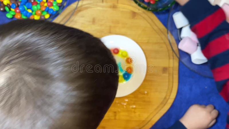 Experimentación con niños. caramelos coloridos en el plato blanco derritiéndose en un arcoiris