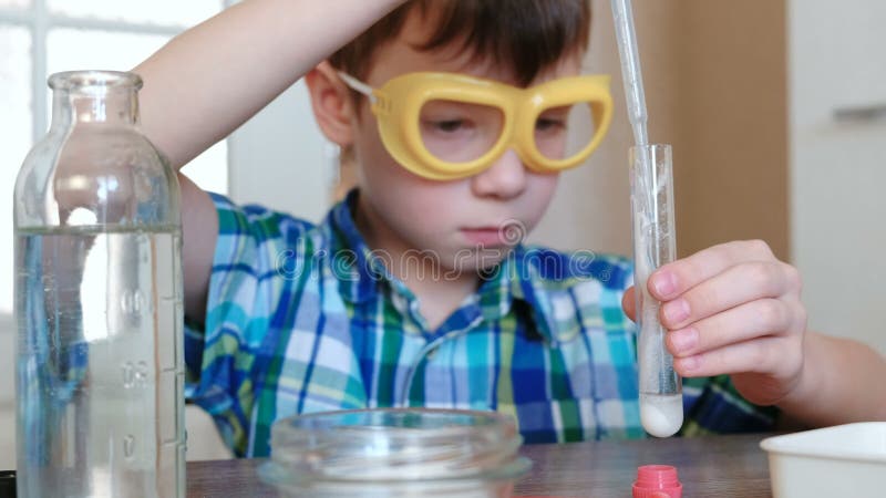 Experiências na química em casa O menino derrama a água no tubo de ensaio com pó usando a pipeta