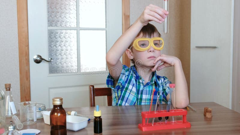 Experiências na química em casa O menino está olhando o tubo para certificar-se d o ` s limpo