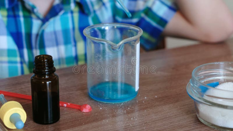 Experiências na química em casa O ` s do menino do close up entrega a misturas as substâncias e o líquido azul na taça usando o v