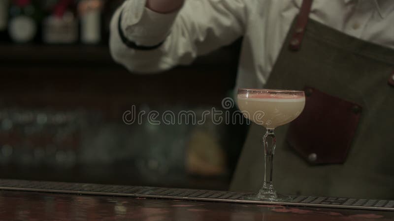 Expert barman is pouring prepared in shaker cocktail to a glass and put it on napkin at night club