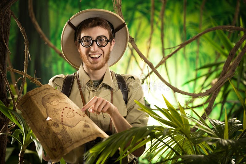 Young smiling explorer in the jungle with thick glasses holding a map.