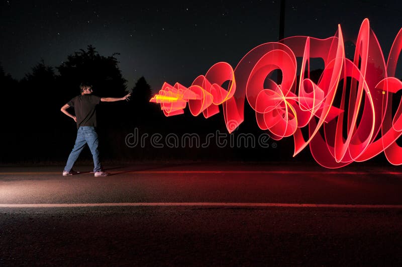 A man in the road at the middle of the night shooting out a graffiti-like artistic laser blast powers from his hand. A man in the road at the middle of the night shooting out a graffiti-like artistic laser blast powers from his hand