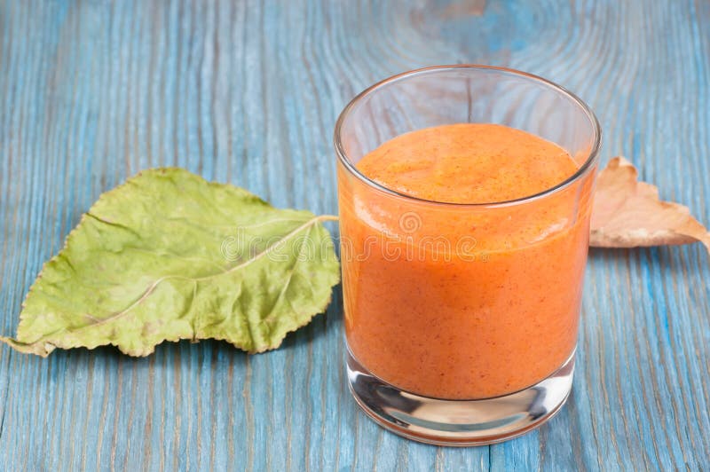 Exponeringsglas av persimonsmoothie och stupade sidor på blått träbräde arkivfoton Exponeringsglas av persimonsmoothie och stupade sidor på blått träbräde arkivfoton