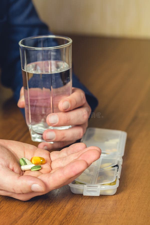 Exponeringsglas av vatten, vitaminer och preventivpillerar för näringsrikt diet-tillägg som rymmer i hand av affärsmannen på arbe royaltyfria bilder Exponeringsglas av vatten, vitaminer och preventivpillerar för näringsrikt diet-tillägg som rymmer i hand av affärsmannen på arbe royaltyfria bilder