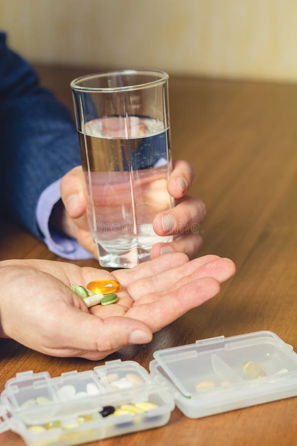 Exponeringsglas av vatten, vitaminer och preventivpillerar för näringsrikt diet-tillägg som rymmer i hand av affärsmannen på arbe royaltyfri fotografi Exponeringsglas av vatten, vitaminer och preventivpillerar för näringsrikt diet-tillägg som rymmer i hand av affärsmannen på arbe royaltyfri fotografi