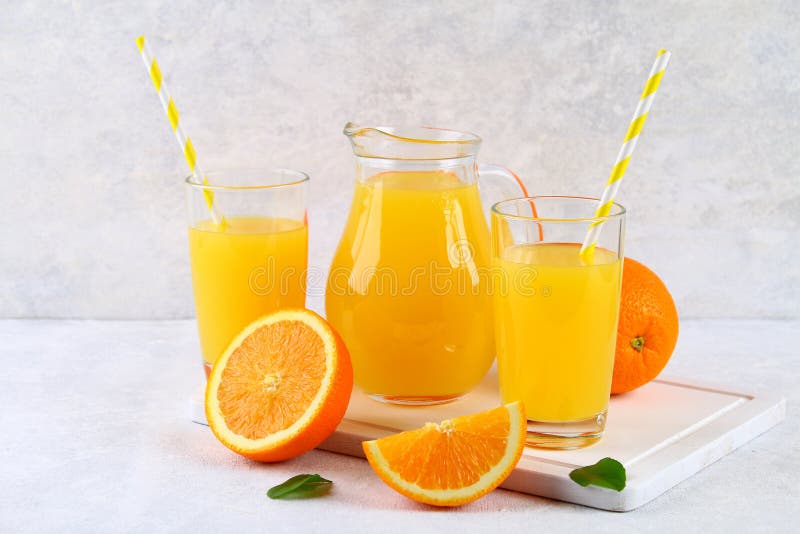 Exponeringsglaskoppar och en kanna av ny orange fruktsaft med skivor av apelsin- och gulingrör på ett ljus - grå tabell fotografering för bildbyråer Exponeringsglaskoppar och en kanna av ny orange fruktsaft med skivor av apelsin- och gulingrör på ett ljus - grå tabell fotografering för bildbyråer