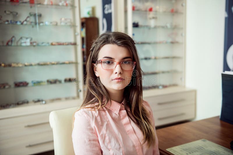 Exponeringsglasändring hur folket ser oss Stående av strikt och allvarligt europeiskt brunettsammanträde i optikerlager in royaltyfria foton Exponeringsglasändring hur folket ser oss Stående av strikt och allvarligt europeiskt brunettsammanträde i optikerlager in royaltyfria foton