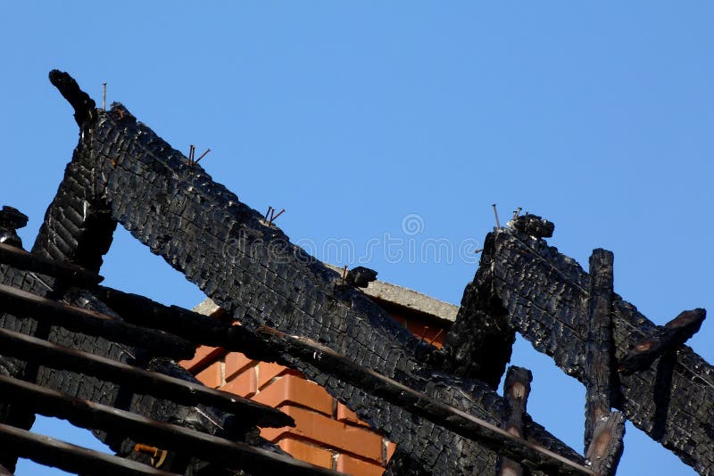 Exposed charred burnt black timber roof structure after house fire. abstract view of rafters under blue sky. fire safety and insurance concept. fire hazard, flammable materials in construction. Exposed charred burnt black timber roof structure after house fire. abstract view of rafters under blue sky. fire safety and insurance concept. fire hazard, flammable materials in construction.