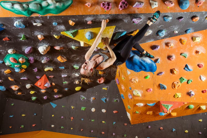 Expressive young woman bouldering in climbing gym