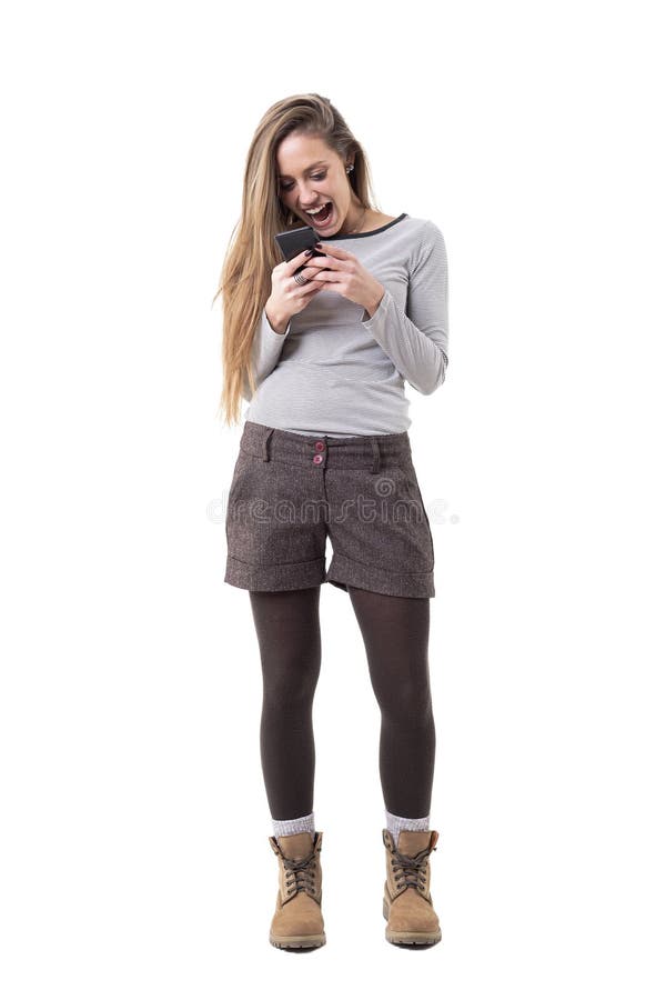 Overjoyed young stylish woman screaming while reading and holding mobile phone. Full body isolated on white background. Overjoyed young stylish woman screaming while reading and holding mobile phone. Full body isolated on white background