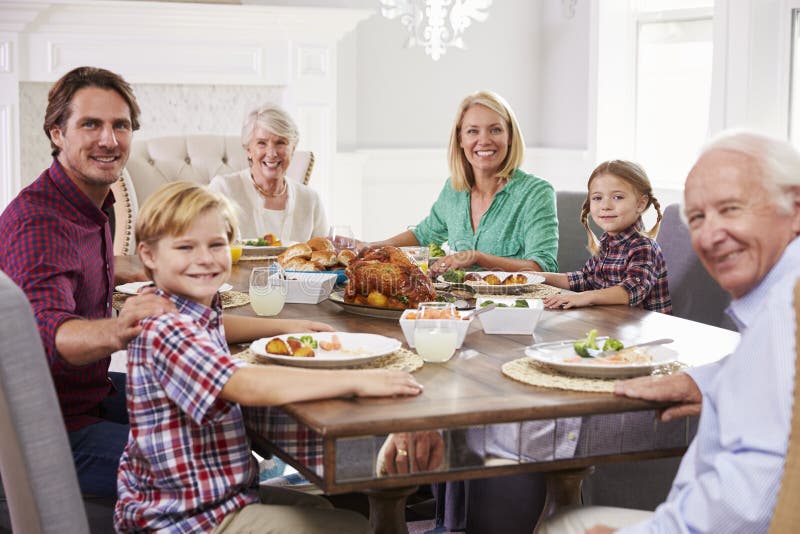Extended Family Group Sit Around Table Eating Meal at Home Stock Image