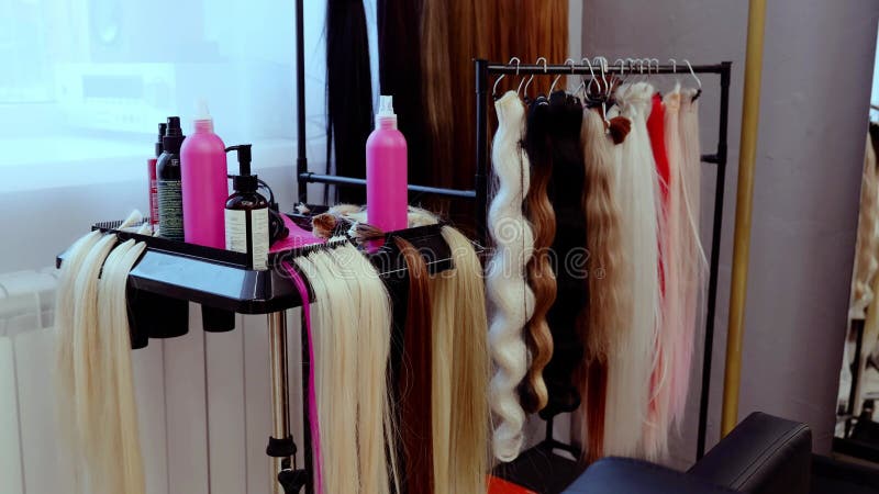 Extensiones de cabello cuelgan en un rack mientras un peluquero selecciona opciones para un cliente en un salón con una botella de almacen de video