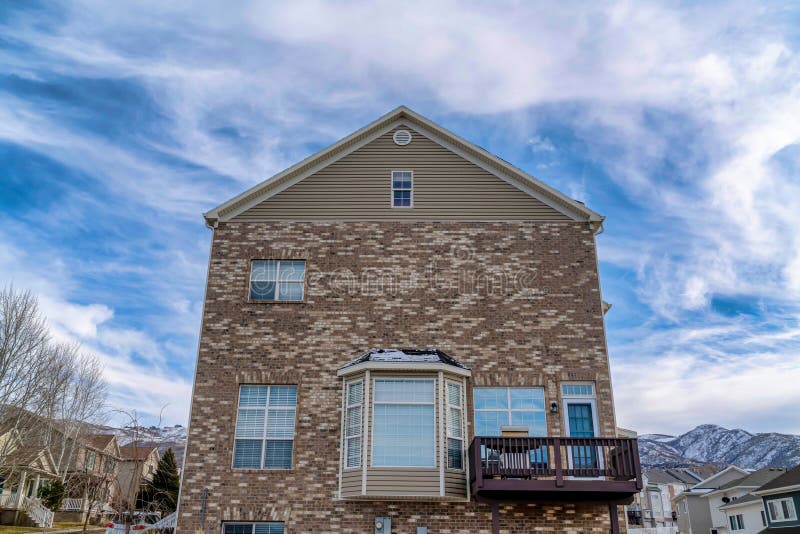 Exterior of house with gable roof and brick wall against blue sky and clouds