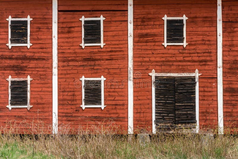 Exterior of old abandoned decayed red barn with closed wooden window shutters.