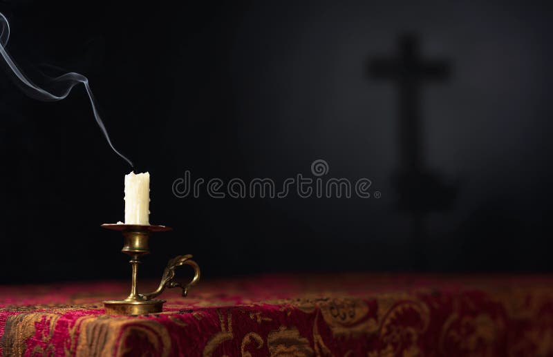 Extinguished candle on a dark background with the silhouette of a cross, selective focus