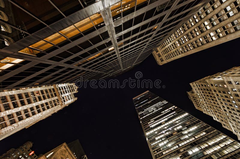 Seen here within the Financial District of Lower Manhattan in New York City are surrounding buildings viewed through a ultra wide angle lens. Take note of the many windows that are lit up under the night sky. Seen here within the Financial District of Lower Manhattan in New York City are surrounding buildings viewed through a ultra wide angle lens. Take note of the many windows that are lit up under the night sky.