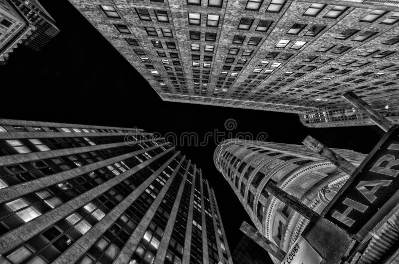 At this particular corner of lower Manhattan the surrounding buildings and skyscrapers meet at just the interesting angles to make for an even more interesting sky view from the street. Shot in Black in White with the occasional window lit up in the night sky. At this particular corner of lower Manhattan the surrounding buildings and skyscrapers meet at just the interesting angles to make for an even more interesting sky view from the street. Shot in Black in White with the occasional window lit up in the night sky.