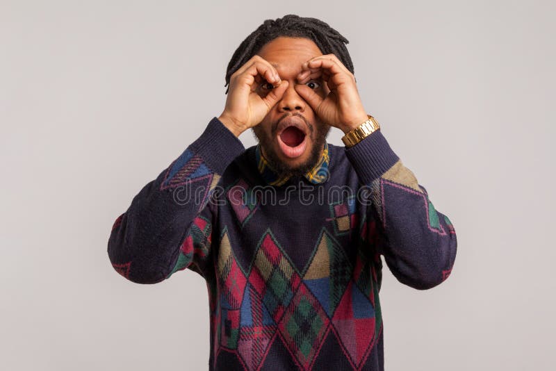 Extremely shocked surprised african guy with dreadlocks looking through fingers with opened mouth imagine binoculars, amazed with royalty free stock photos