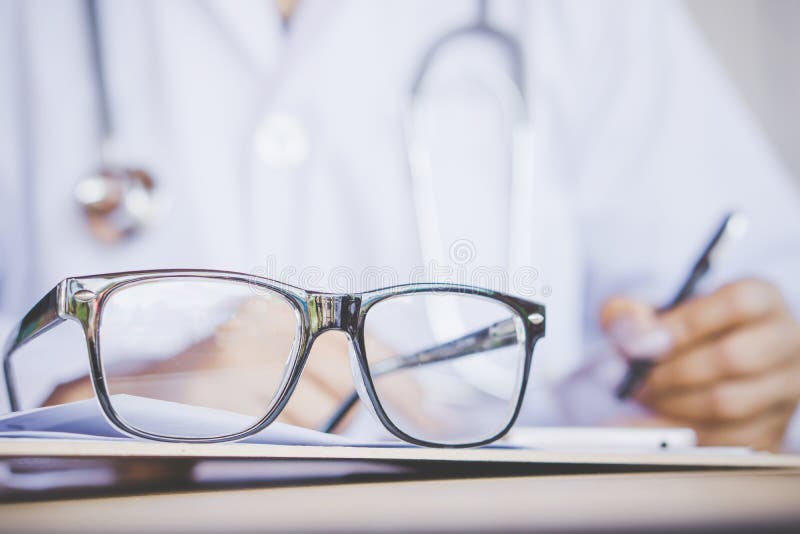 Eye glasses on desk with blur background of doctor writing prescription