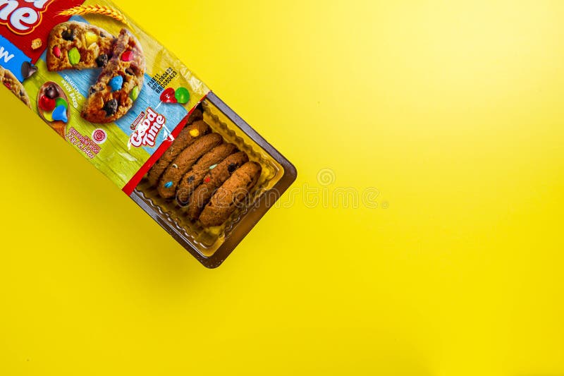 An eye-level studio shot featuring a package of colorful Good Time Rainbow Cookies, some in the package and some in the tray, against a solid yellow background.