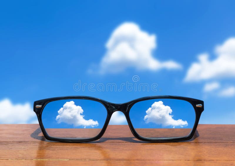 Eyeglasses on Wooden Table Front of Abstract White Clouds Stock Photo