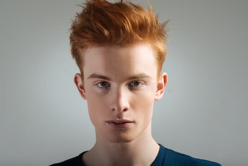 Stony-faced red-haired young man staring