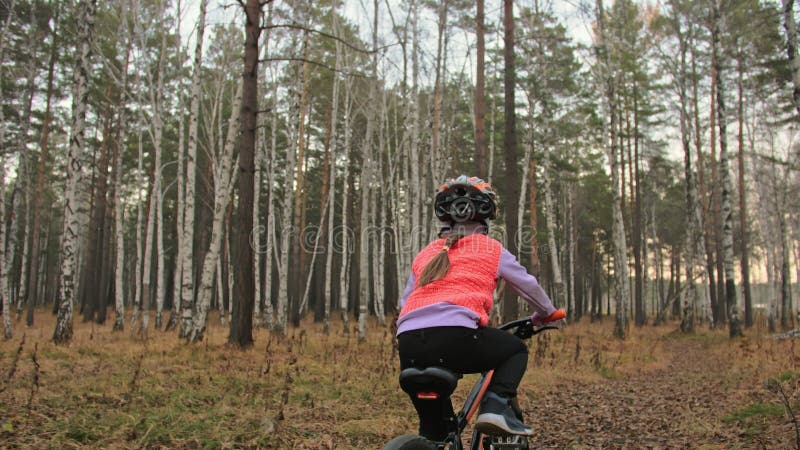 Eén kaukasische kinderfietsweg in het herfstpark Klein meisje met zwarte oranje cyclus in het bos Kid doet het wel