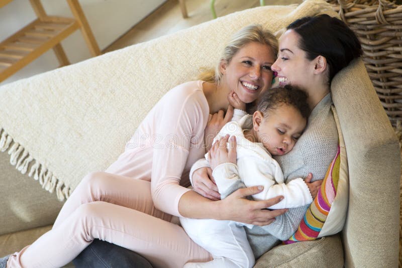 Same sex female couple cuddling on the sofa with their sleeping son. Same sex female couple cuddling on the sofa with their sleeping son