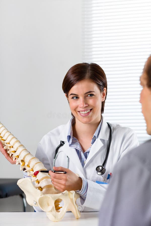 Female Orthopaedic surgeon explaining a back injury or disease to a male patient on crutches with the help of a human spine. Female Orthopaedic surgeon explaining a back injury or disease to a male patient on crutches with the help of a human spine