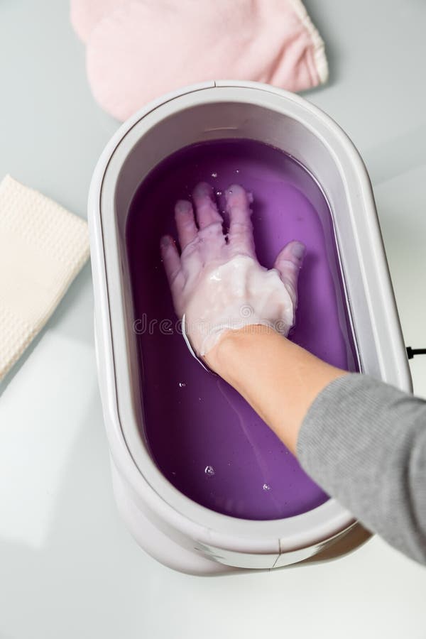 Female hands taking procedure in a lilac paraffin wax bowl. Cosmetological and skincare equipment in a beauty & spa salon. Female hands taking procedure in a lilac paraffin wax bowl. Cosmetological and skincare equipment in a beauty & spa salon.