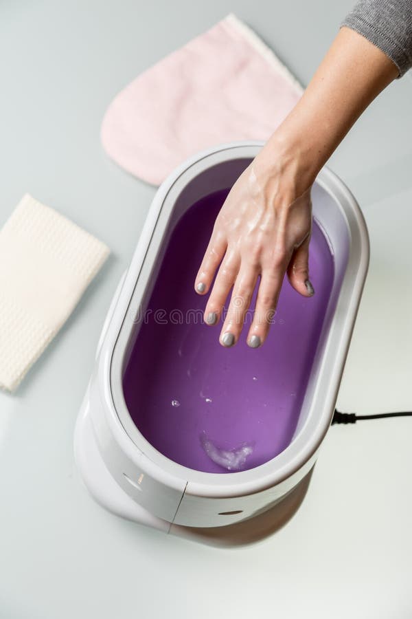 Female hands taking procedure in a lilac paraffin wax bowl. Cosmetological and skincare equipment in a beauty & spa salon. Female hands taking procedure in a lilac paraffin wax bowl. Cosmetological and skincare equipment in a beauty & spa salon.