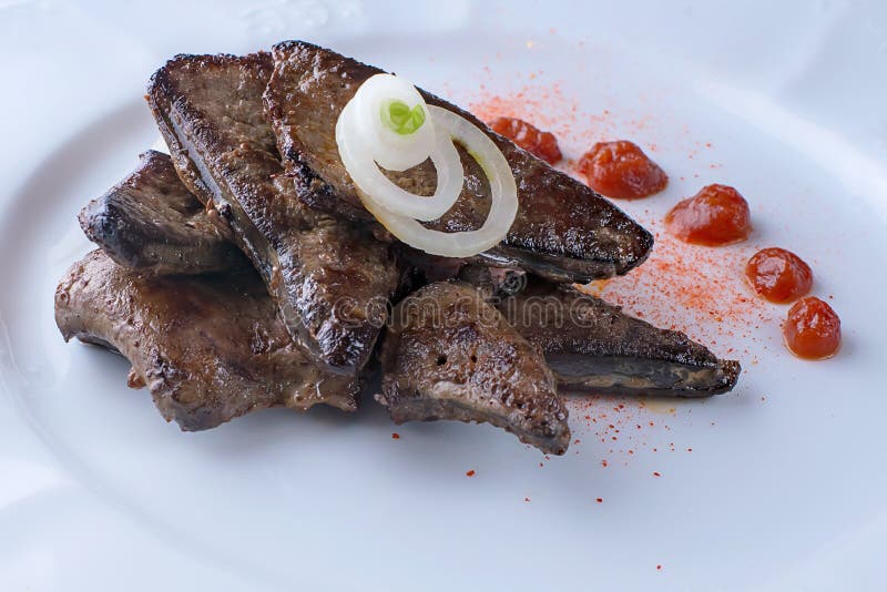 Fígado frito e cebola em uma panela, com mostarda e ketchup, em uma mesa  escura, vista de cima.