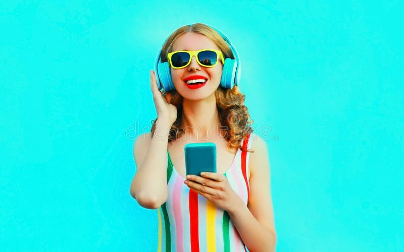 F?r kvinnainnehav f?r st?ende som lycklig le telefon lyssnar till musik i tr?dl?s h?rlurar p? f?rgrika bl?tt arkivfoton F?r kvinnainnehav f?r st?ende som lycklig le telefon lyssnar till musik i tr?dl?s h?rlurar p? f?rgrika bl?tt arkivfoton