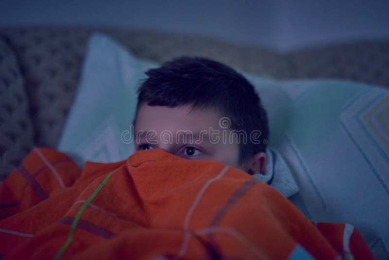 F?rskr?ckt barn som h?ller ?gonen p? l?skig film p? tv som sitter p? soffan p? natten arkivfoton F?rskr?ckt barn som h?ller ?gonen p? l?skig film p? tv som sitter p? soffan p? natten arkivfoton