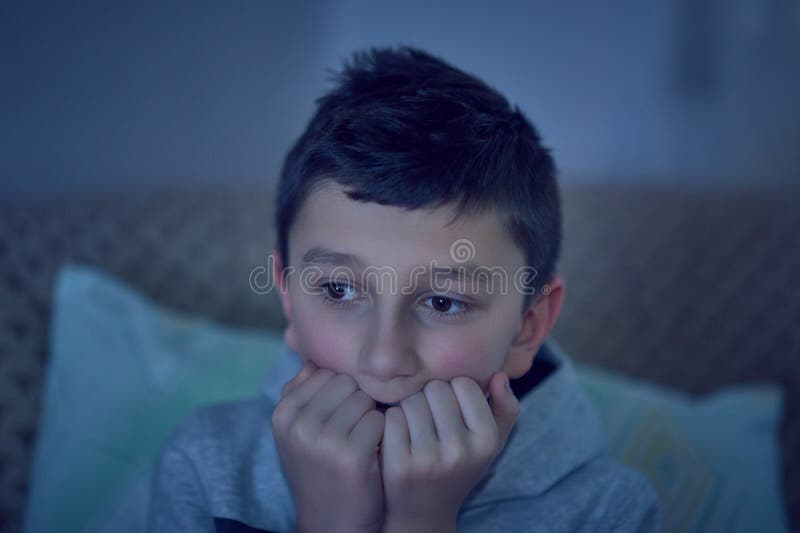 F?rskr?ckt barn som h?ller ?gonen p? l?skig film p? tv som sitter p? soffan p? natten fotografering för bildbyråer F?rskr?ckt barn som h?ller ?gonen p? l?skig film p? tv som sitter p? soffan p? natten fotografering för bildbyråer