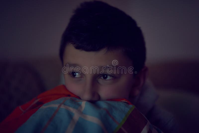 F?rskr?ckt barn som h?ller ?gonen p? l?skig film p? tv som sitter p? soffan p? natten arkivbilder F?rskr?ckt barn som h?ller ?gonen p? l?skig film p? tv som sitter p? soffan p? natten arkivbilder