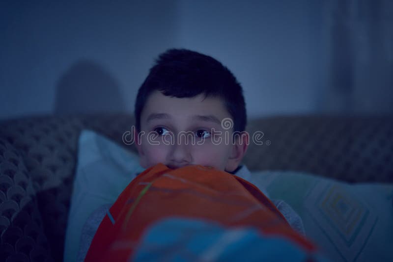 F?rskr?ckt barn som h?ller ?gonen p? l?skig film p? tv som sitter p? soffan p? natten arkivfoton F?rskr?ckt barn som h?ller ?gonen p? l?skig film p? tv som sitter p? soffan p? natten arkivfoton