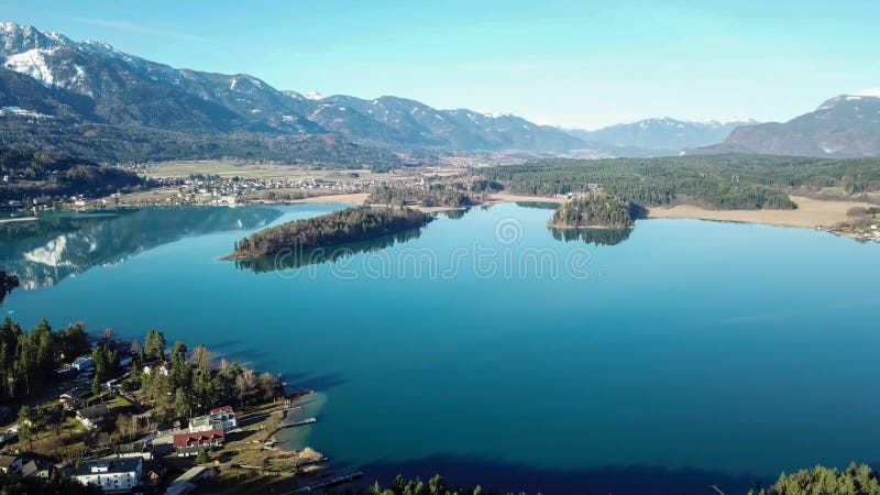 Faakersee - A drone shot of a Faaker lake in Austrian Alps. The lake is surrounded by high mountains. There is a small island