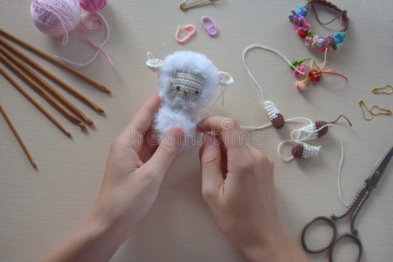 Making fanny sheep with wreath of flowers. Crochet toy ewe for child.  On table threads, needles, hook, cotton yarn. Step 2 - to sew all details of toy. Handmade crafts. DIY concept. Small business. Income from hobby. Making fanny sheep with wreath of flowers. Crochet toy ewe for child.  On table threads, needles, hook, cotton yarn. Step 2 - to sew all details of toy. Handmade crafts. DIY concept. Small business. Income from hobby