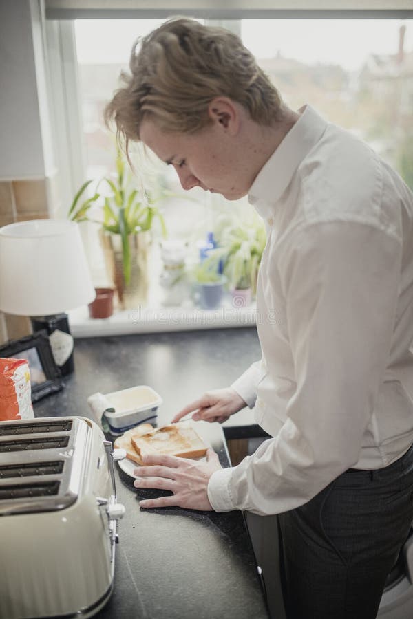 Close-up, side angle view of a young adult businessman making toast for his breakfast before work. Close-up, side angle view of a young adult businessman making toast for his breakfast before work.