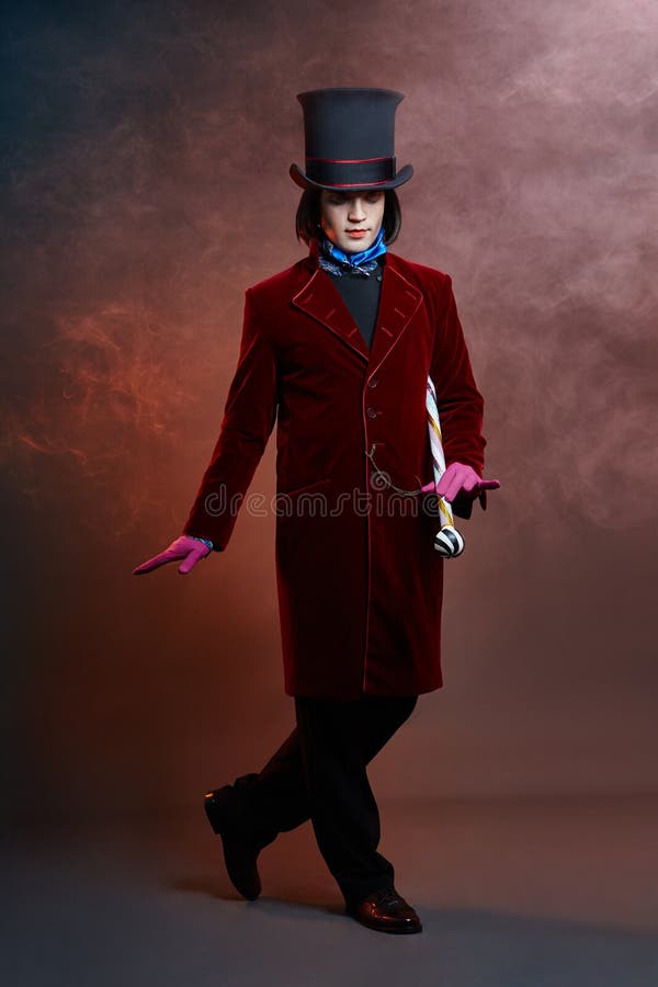 Fabulous circus man in a hat and a red suit posing in the smoke on a colored dark background. A clown at a party, man gentleman