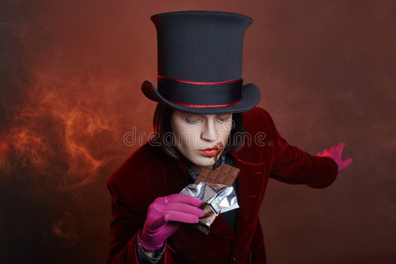 Fabulous circus man in a hat and a red suit posing in the smoke on a colored dark background. A clown at a party, man gentleman