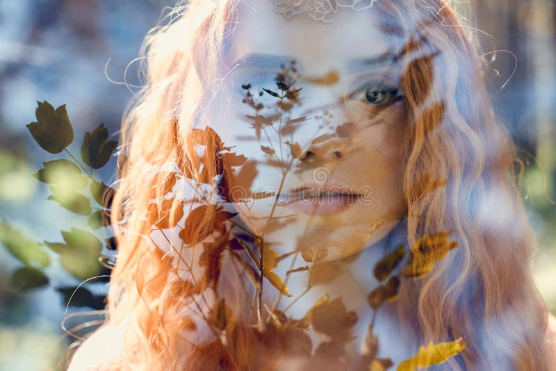 Fabulous portrait of a red-haired girl in nature with double exposure and glare. Beautiful redhead girl with long hair in forest