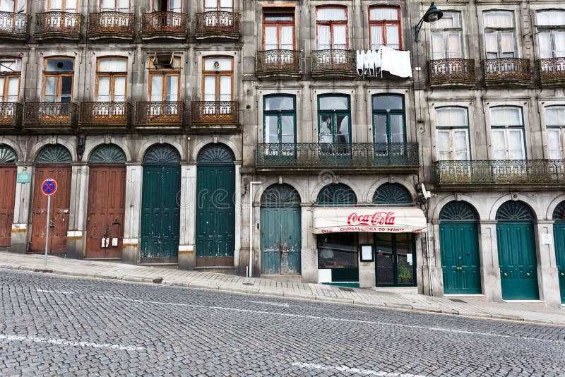 Facade of the lower stories of an apartment house on a steeply sloped cobblestone street in Porto, Portugal