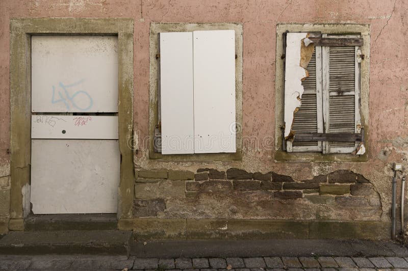 Facciata della casa abbandonata, imbarcata-su, dilapidata con la porta e di 2 finestre con gli otturatori immagine stock libera da diritti Facciata della casa abbandonata, imbarcata-su, dilapidata con la porta e di 2 finestre con gli otturatori immagine stock libera da diritti