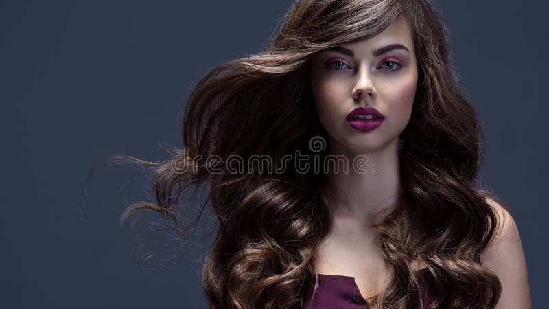 Face of a beautiful woman with long brown curly hair. Fashion model with wavy hairstyle. Attractive young  girl with curly hair