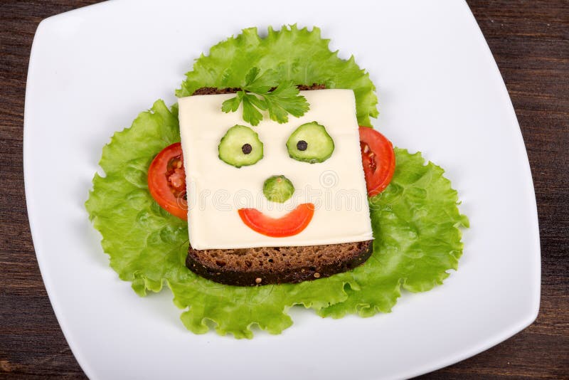 Face on bread, made from cheese, lettuce, tomato, cucumber and pepper.