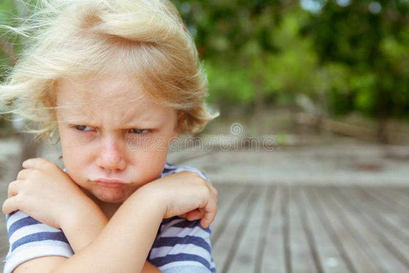 Face portrait of annoyed and unhappy caucasian kid with crossed arms. Upset and angry child concept for family relations, social problems issues and juvenile psychology. Copy space outdoor background. Face portrait of annoyed and unhappy caucasian kid with crossed arms. Upset and angry child concept for family relations, social problems issues and juvenile psychology. Copy space outdoor background